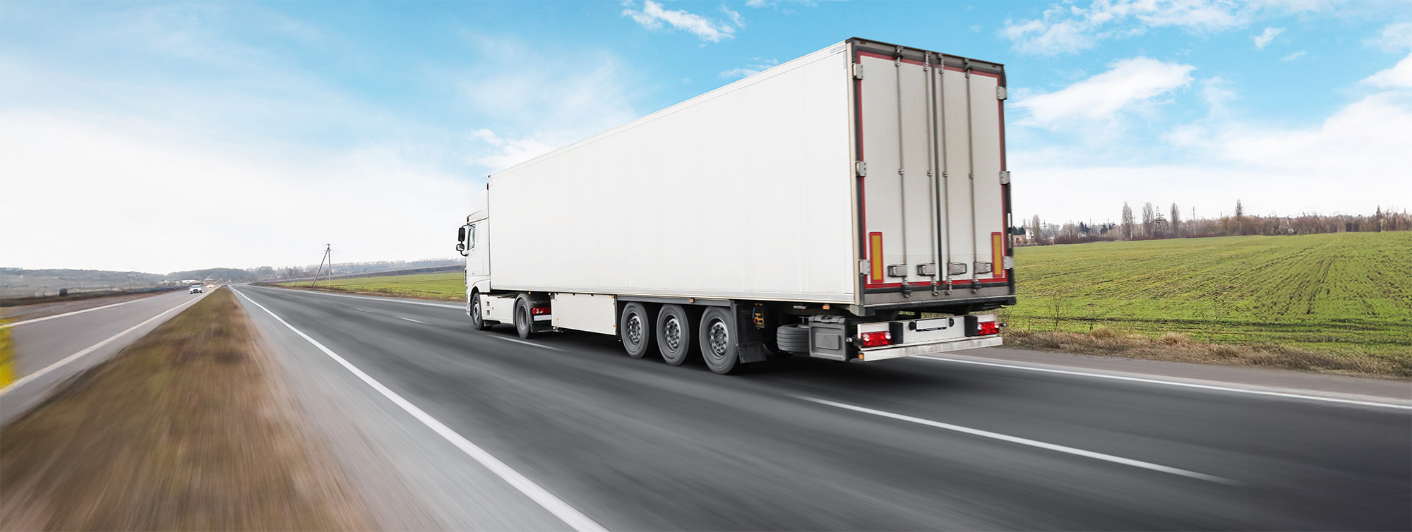 big truck and a trailer on the countryside road in motion against a blue sky with clouds