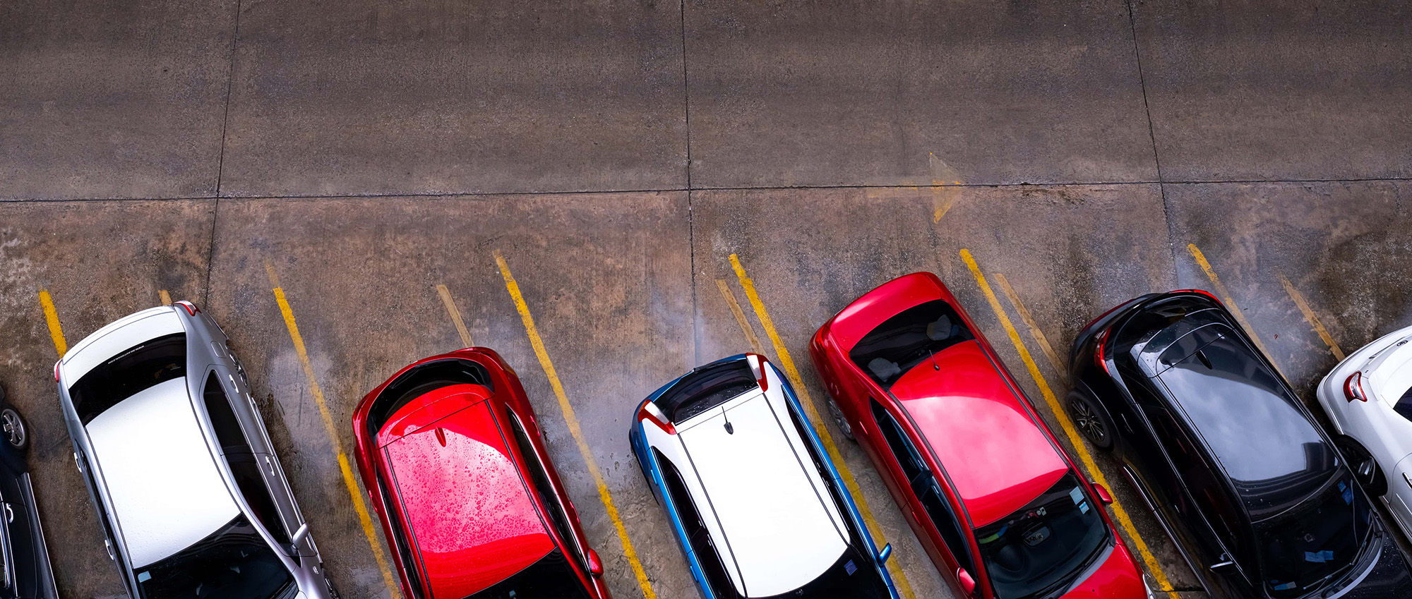 top view of car parked at concrete car parking lot with yellow line of traffic sign on the street. above view of car in a row at parking space
